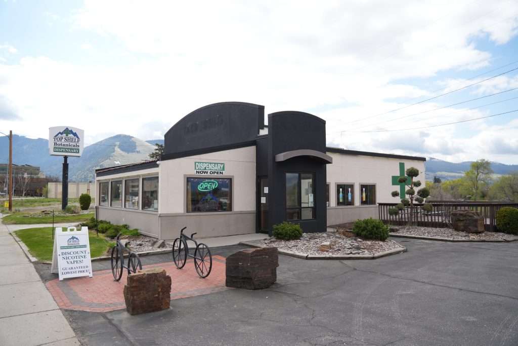 Exterior of Missoula dispensary on Broadway, MT, with cannabis signage and parking area.