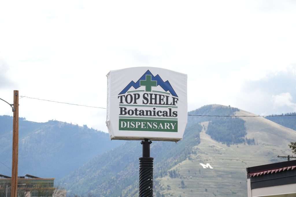Exterior of Missoula dispensary on Broadway, MT, with cannabis signage and parking area.