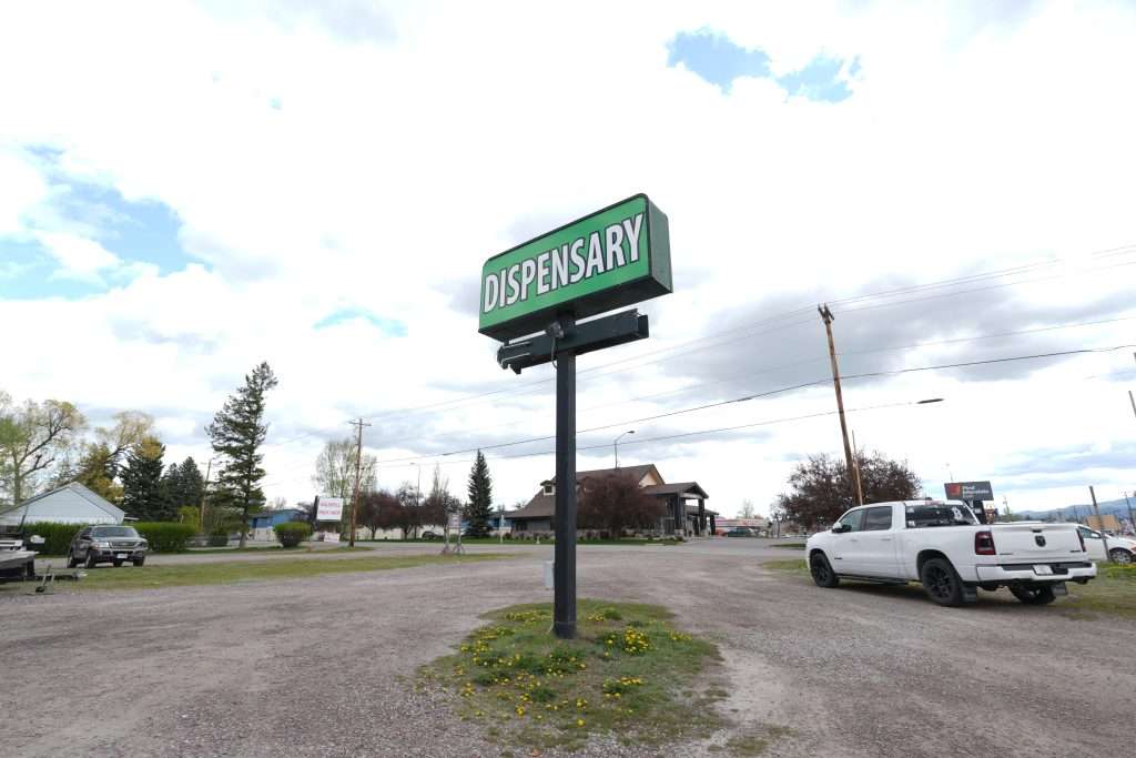 Exterior of dispensary in Kalispell, MT, with a visible cannabis sign and parking area.