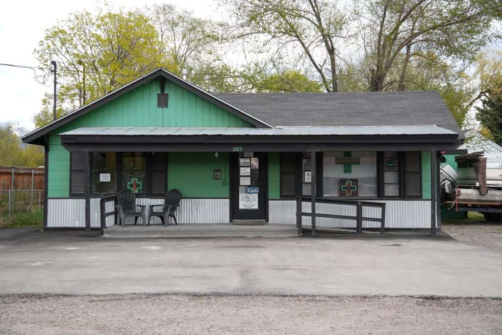 Exterior of dispensary in Kalispell, MT, with a visible cannabis sign and parking area.